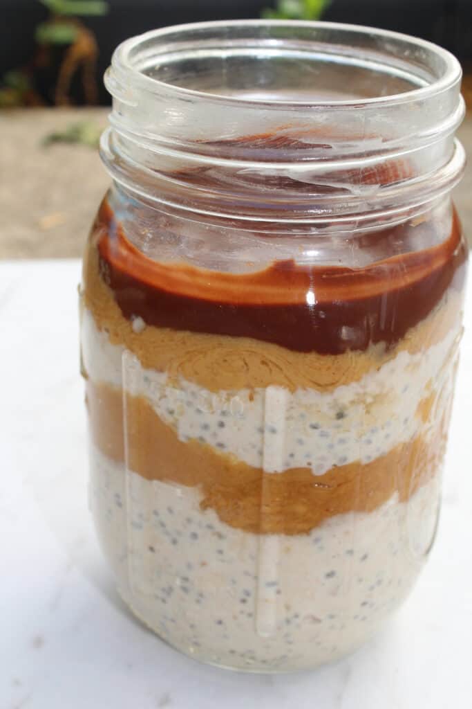 Mason jar of chocolate peanut butter snickers overnight oats with caramel layer