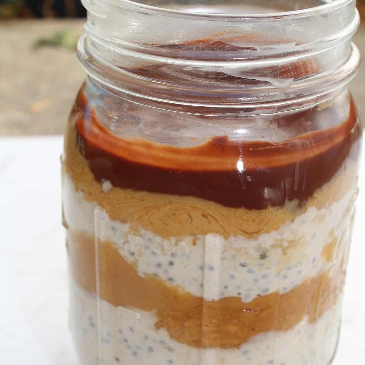 Mason jar of chocolate peanut butter snickers overnight oats with caramel layer