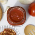 Low sodium pizza sauce recipe in a jar with tomato and red crushed pepper on a table