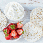 rice cake ideas for weight loss image of ricotta cheese in a bowl, sliced strawberries and rice cakes.